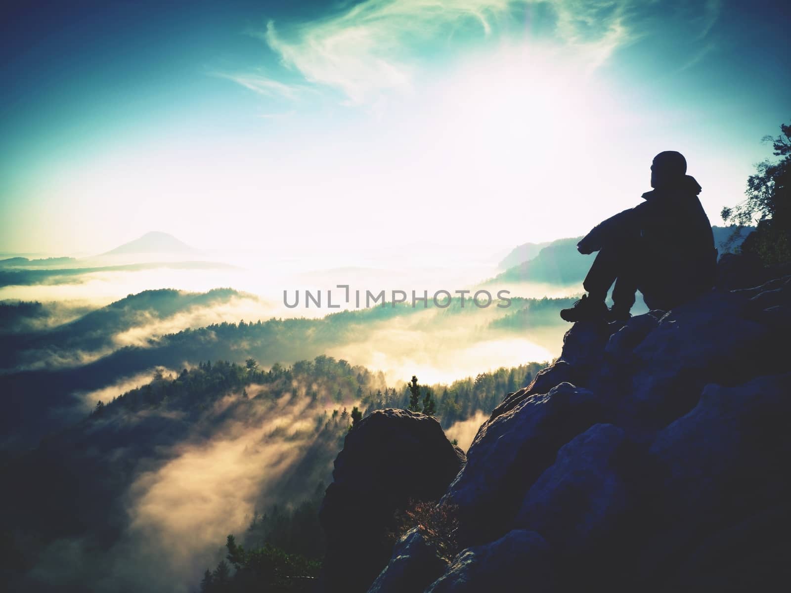 Hiker man take a rest on mountain peak. Man lay on summit, bellow autumn valley. Bright morning Sun shining in sky. 