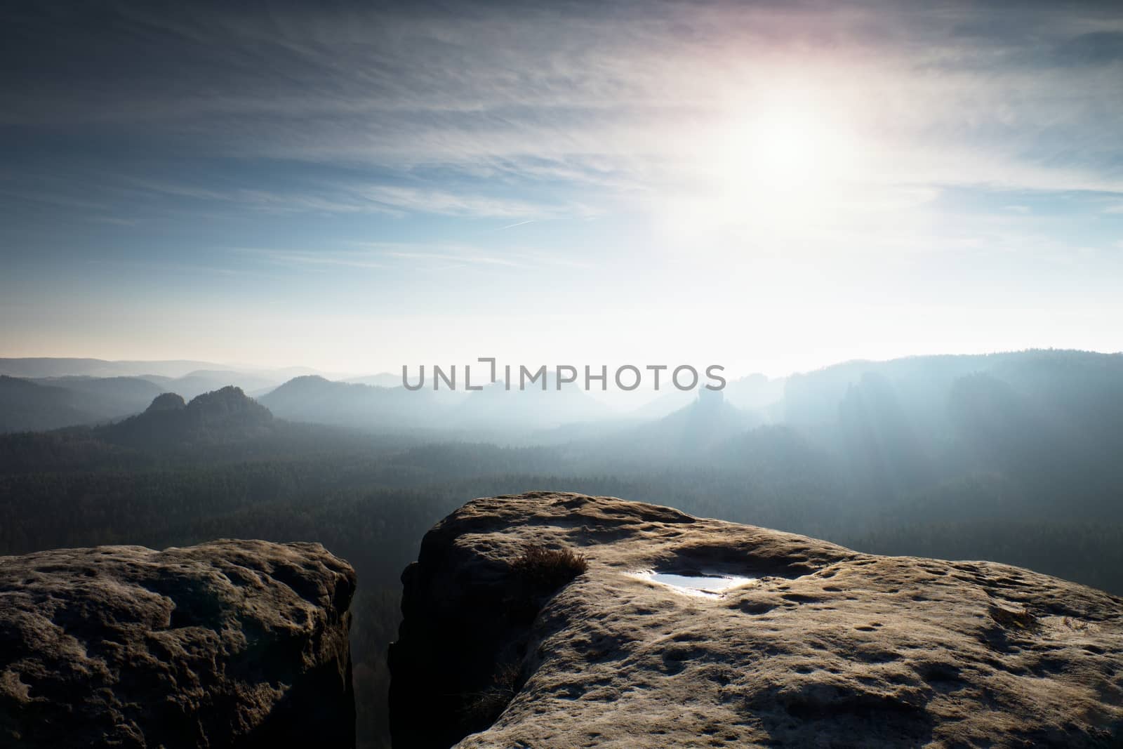 Blue spring daybreak. Sandstone cliff above deep misty valley in Saxony Switzerland. Hilly peaks sticking out from sreamy fog.
