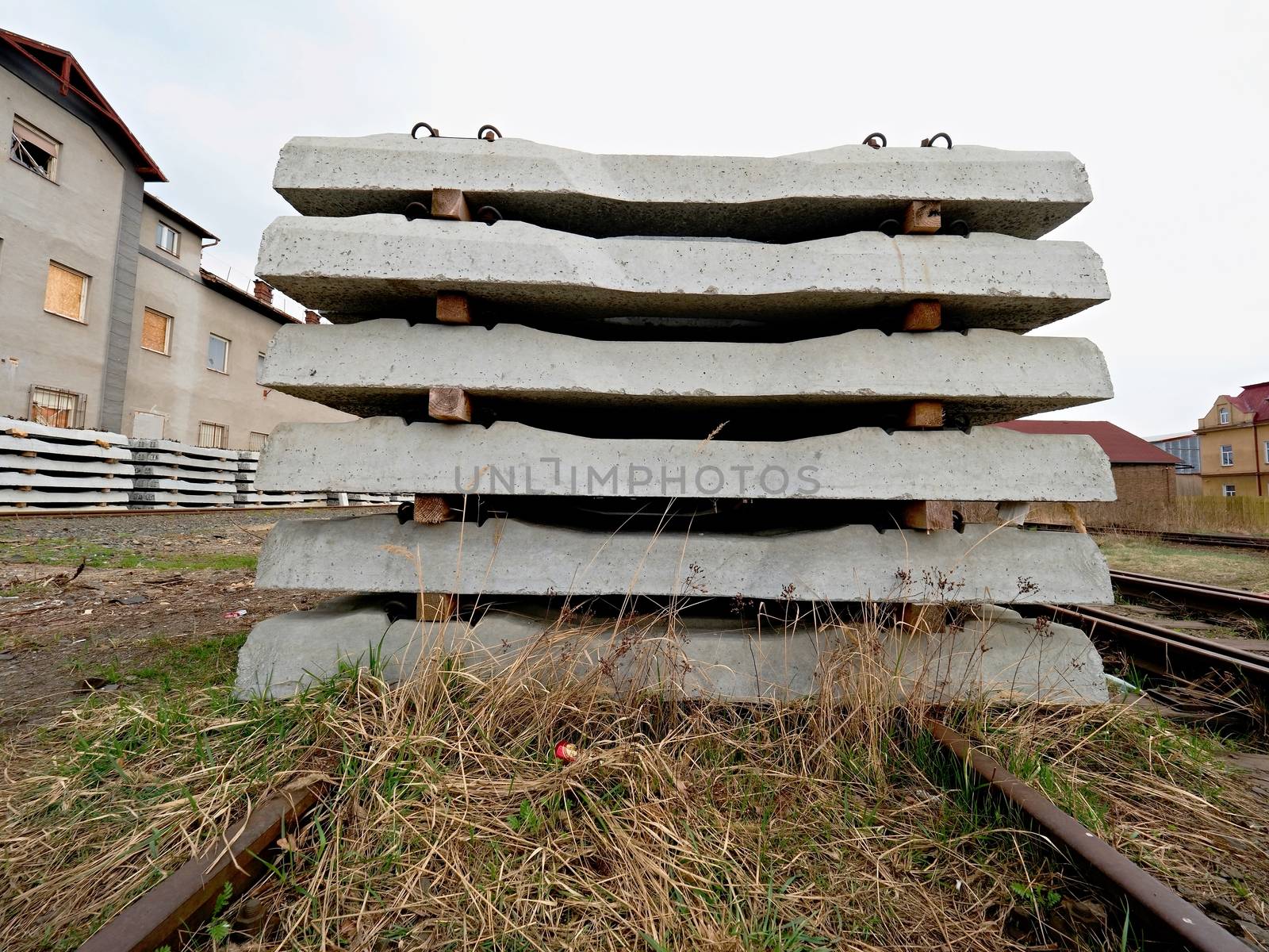 Sleepers stock in railway depot. New concrete railway ties stored for reconstruction of old railway station. Old houses  in background