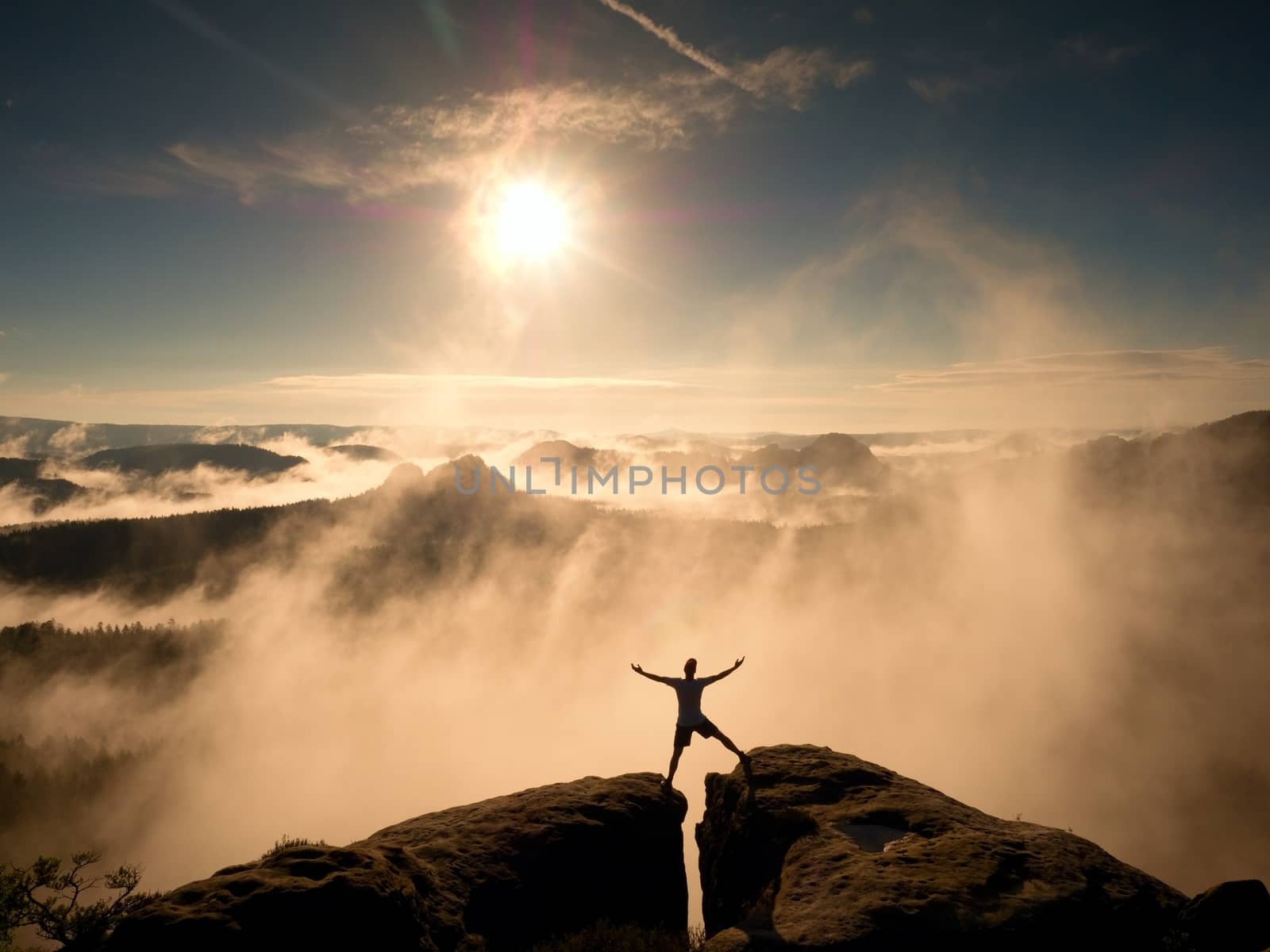 Mountain summit. Happy man gesture raised arms. Funny hiker with raised hands in the air on rock edge in national park. Vivid and strong vignetting effect.