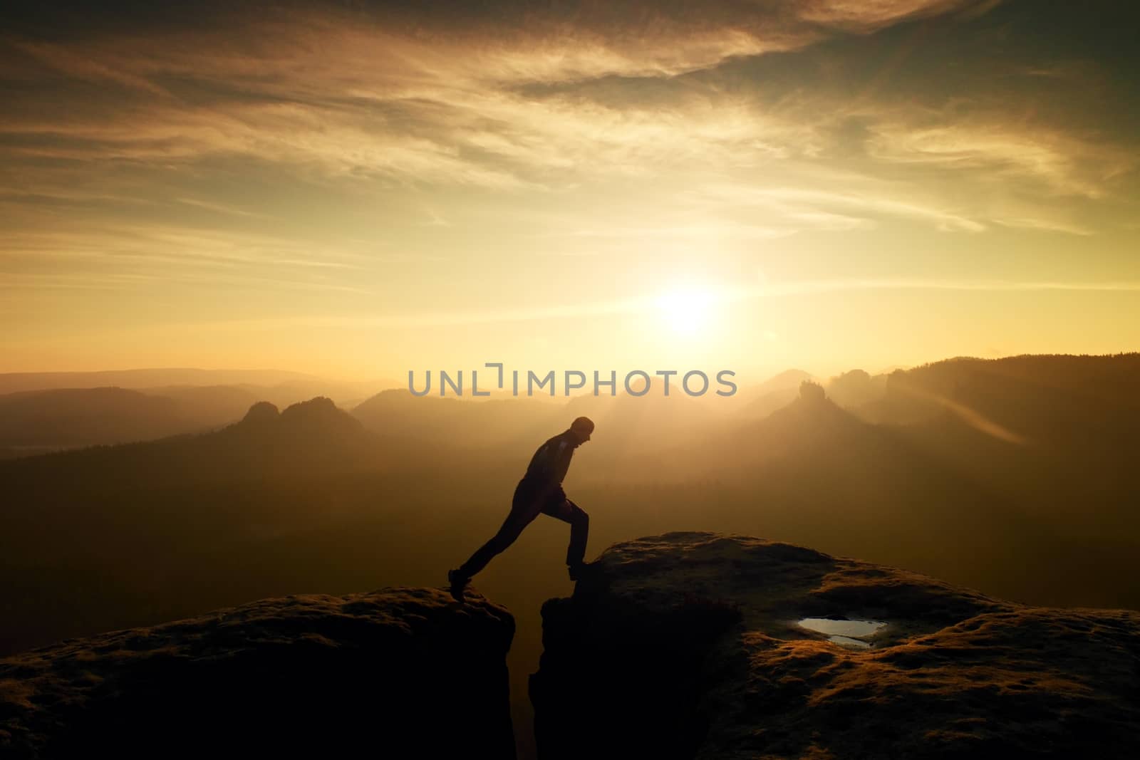 Jumping man. Young man makes jump on colorful sky background in mountains. heavy orange mist in deep valley. Miracle of nature