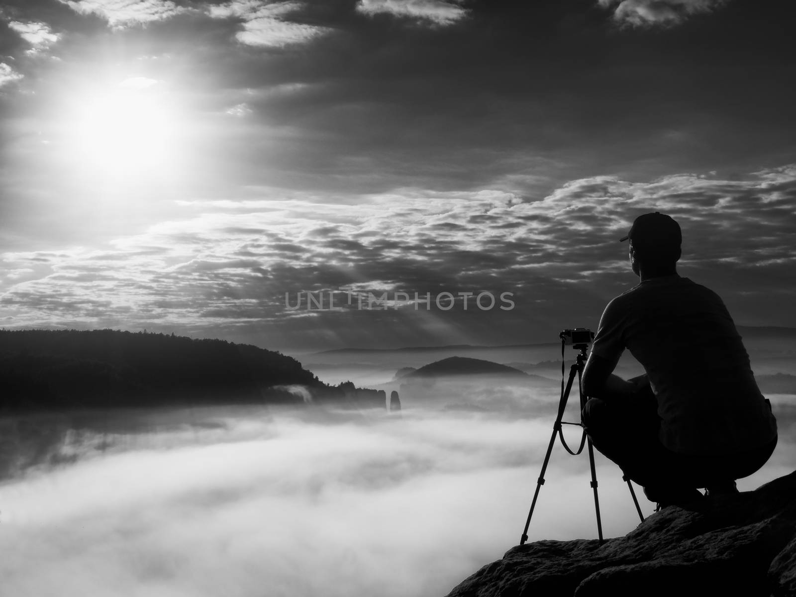 Amateur photographer takes photos with mirror camera on peak of rock. Dreamy fogy landscape, spring orange pink misty sunrise in a beautiful valley below