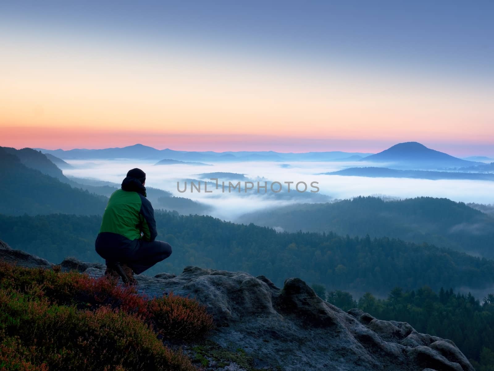 Hiker  man on rock watch over creamy mista and foggy morning landscape. Beautiful fall morning. Autumn hilly cvountryside