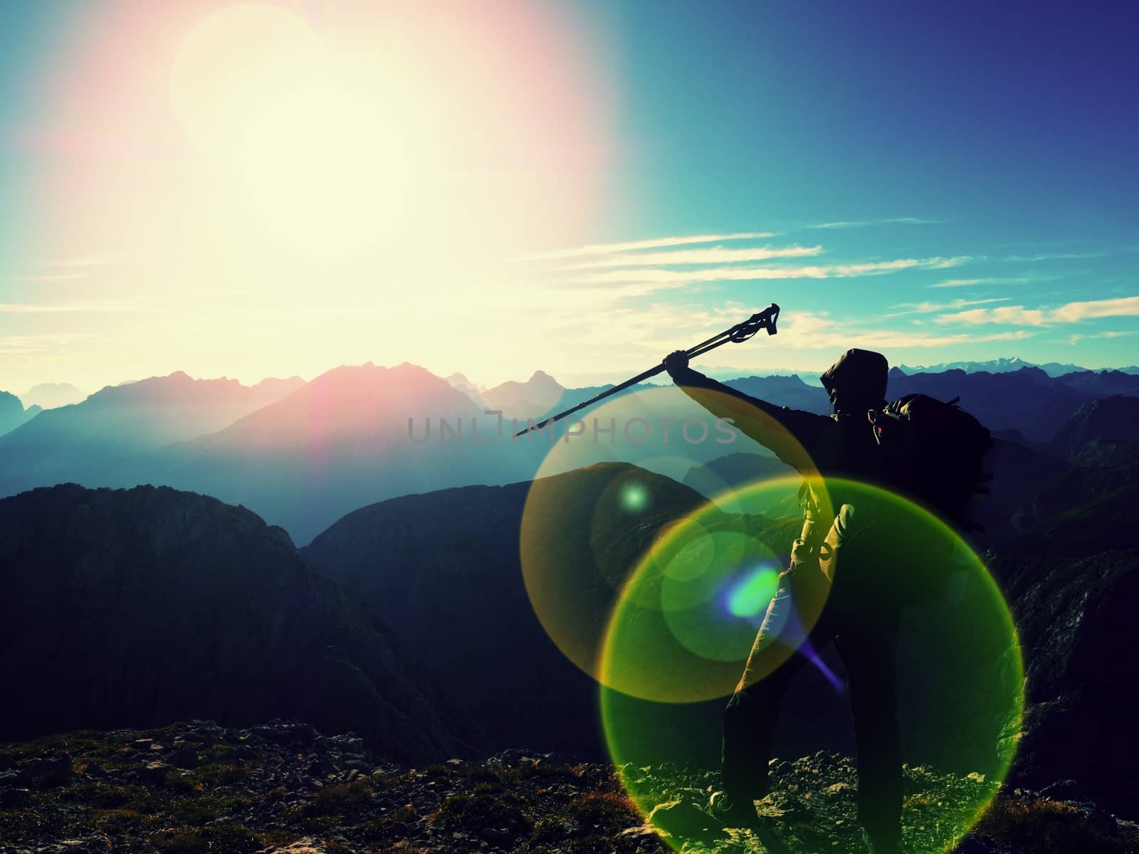Lens flare light, strong defect. Tall backpacker with poles in hand. Sunny weather in rocky mountains. Hiker with big backpack stand on rocky view point above misty valley. 