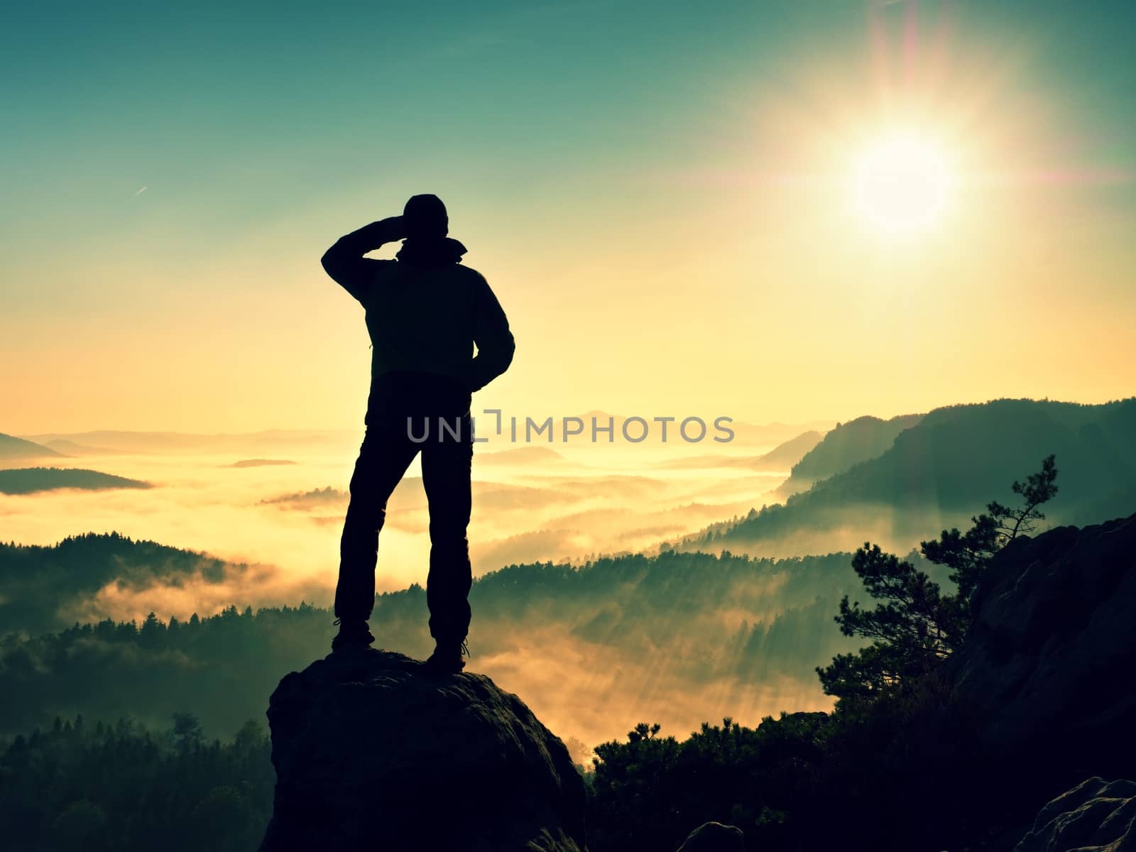 Man silhouette climbing high on cliff. Hiker climbed up to peak enjoy view. Man  watch over misty and foggy morning valley in morning Sun. 
