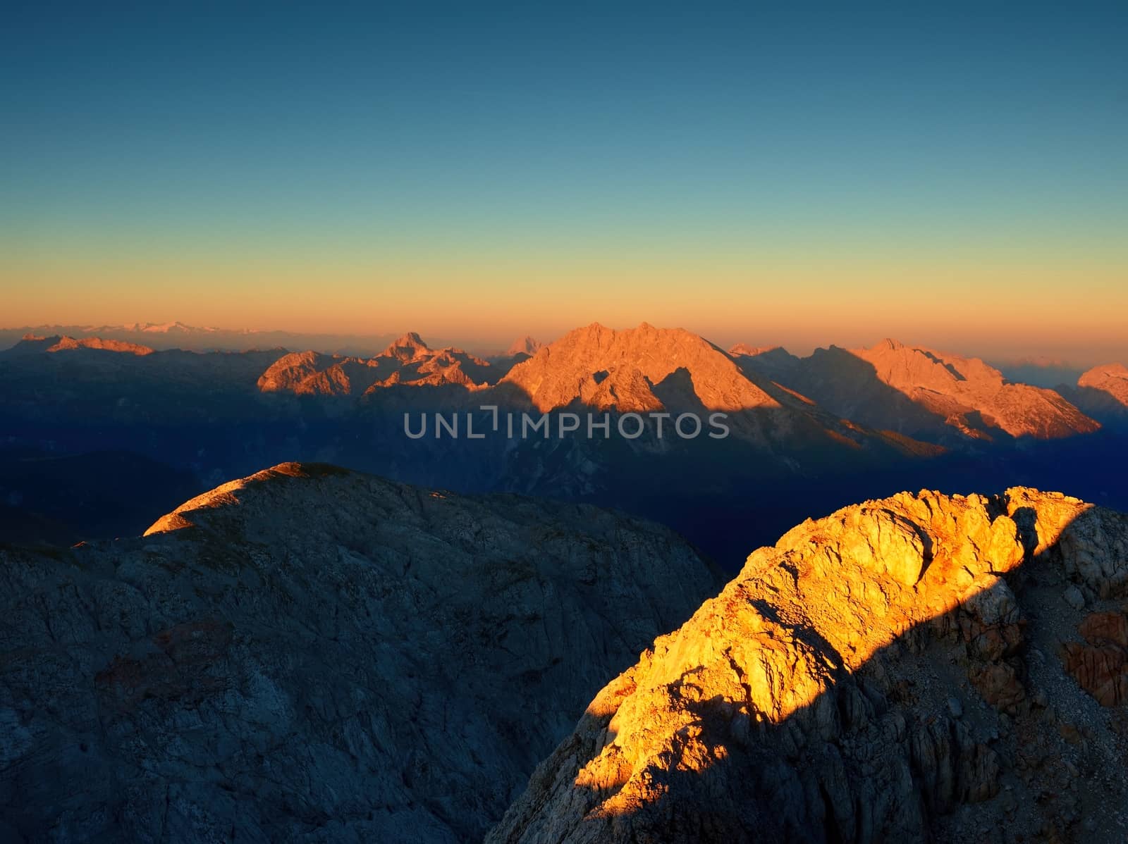 Morning Sun on  Alpine  cliff and night in valley bellow. Daybreak Sun shinning  horizon. Mountains increased from foggy background