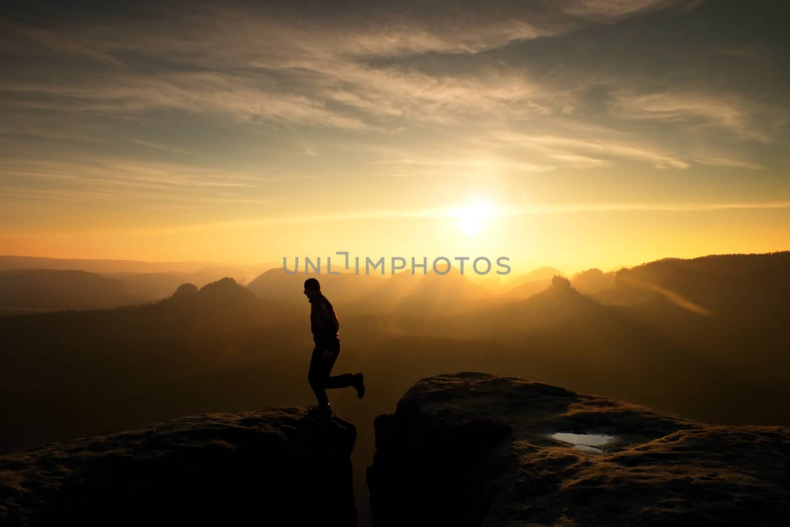 Jumping man. Young man makes jump on colorful sky background in mountains. heavy orange mist in deep valley. Miracle of nature