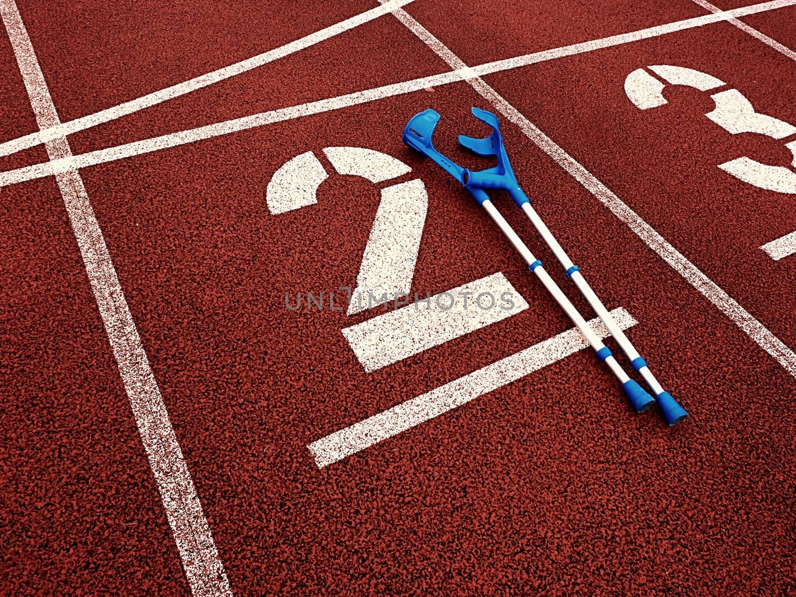 Medicine crutch for broken leg. Number two. Big white track number two on red rubber racetrack. Gentle textured running racetracks in athletic stadium