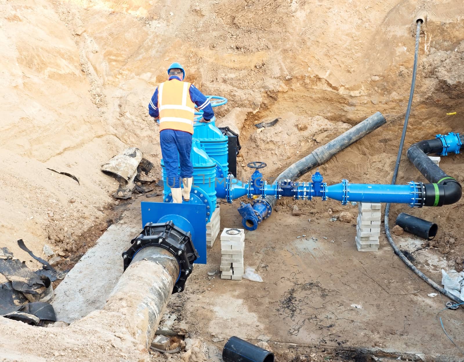 Worker works underground for reconstrucion of drink water system. Technical expert at  gate valve on new pipeline system check of repaired connection before covering by clay