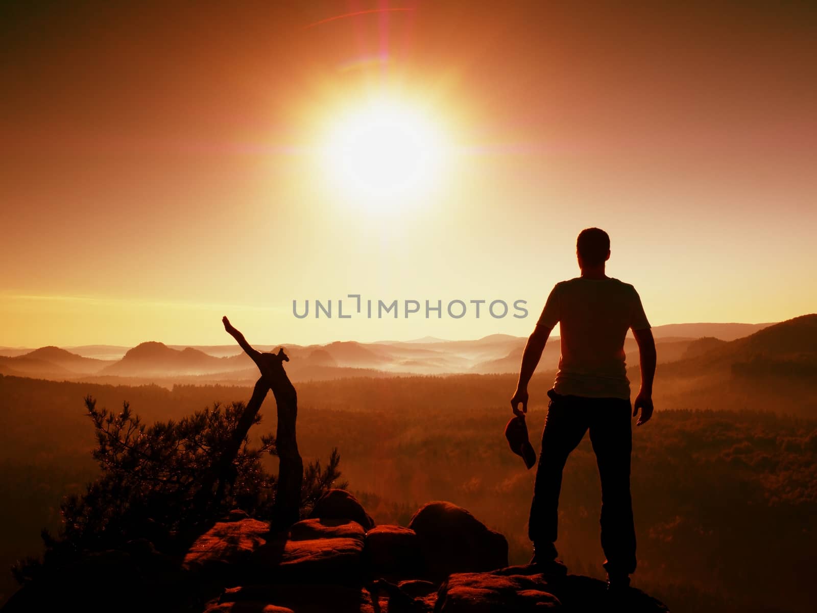 Hiker in grey t-shirt with red  cap in hand stay on rocky peak. Man watching over  valley to Sun. Beautiful moment the miracle of nature. Vintage effect. 