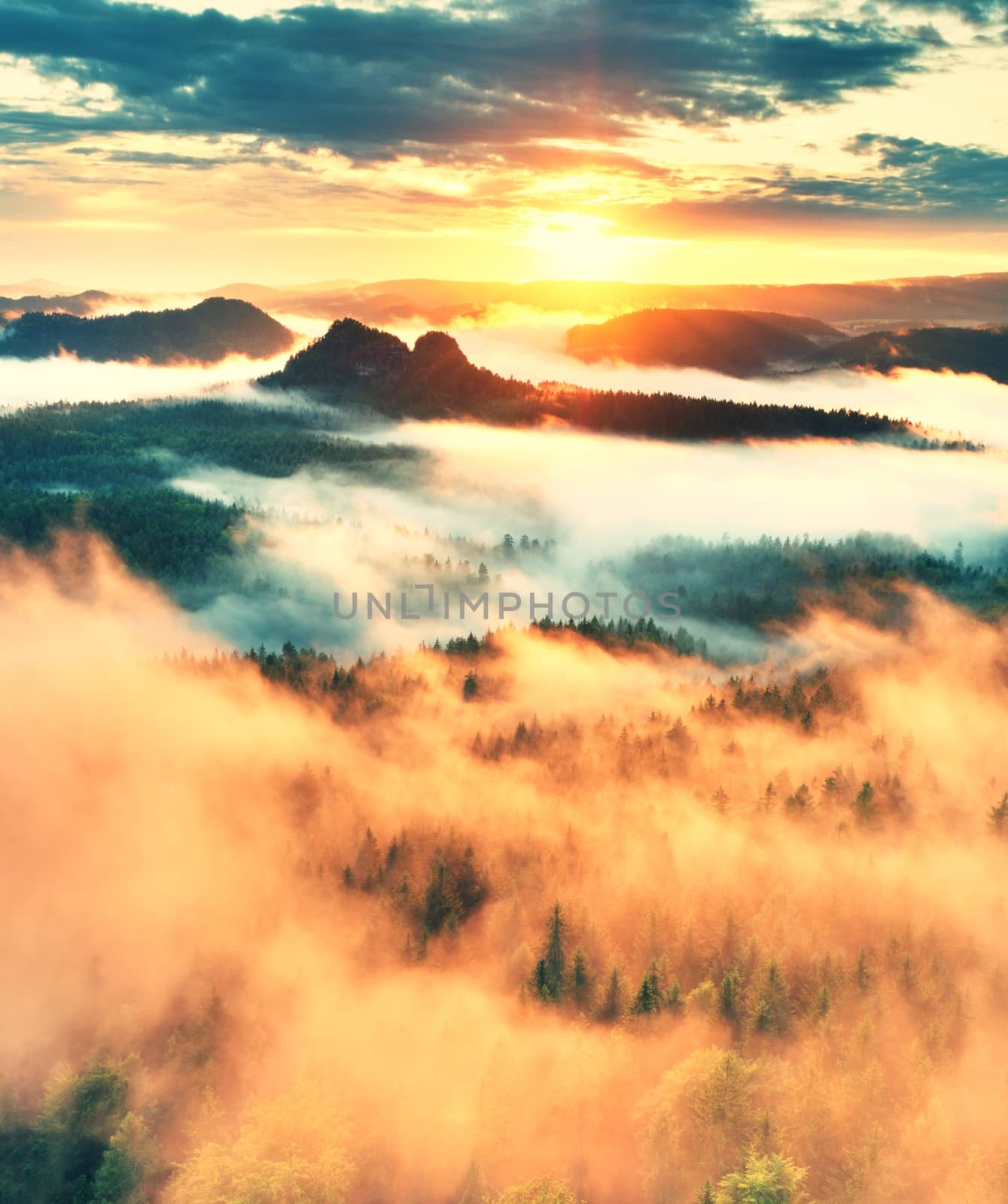 Pink sunrise in a beautiful sandstone rocky mountain. Sharp peaks increased from foggy background, the fog is red and orange due to hot sun rays. 