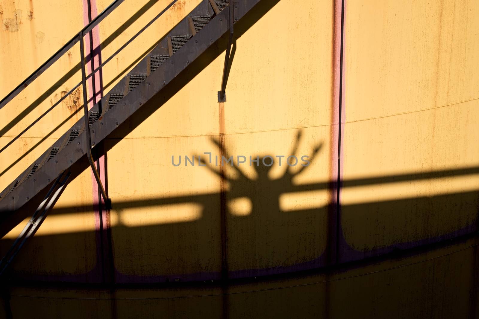 People shadows on old metal tanks in power plant, old kind of factory plant. Metal construction with old yellow paint and rusty places. Iron circle ladders around construction