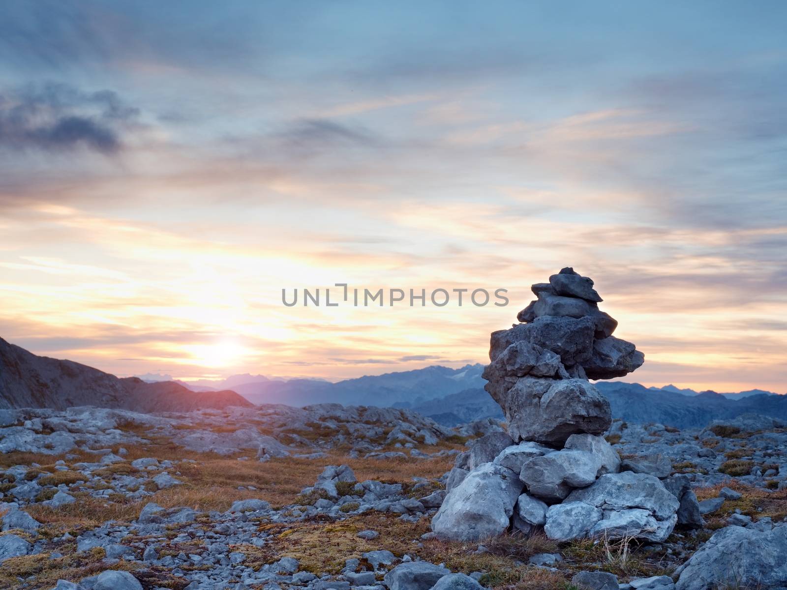 Pebbles pyramid. Stones on Alpine gravel mountain summit. Daybreak horizon above blue foggy valley. Allps mountains increased from humidity