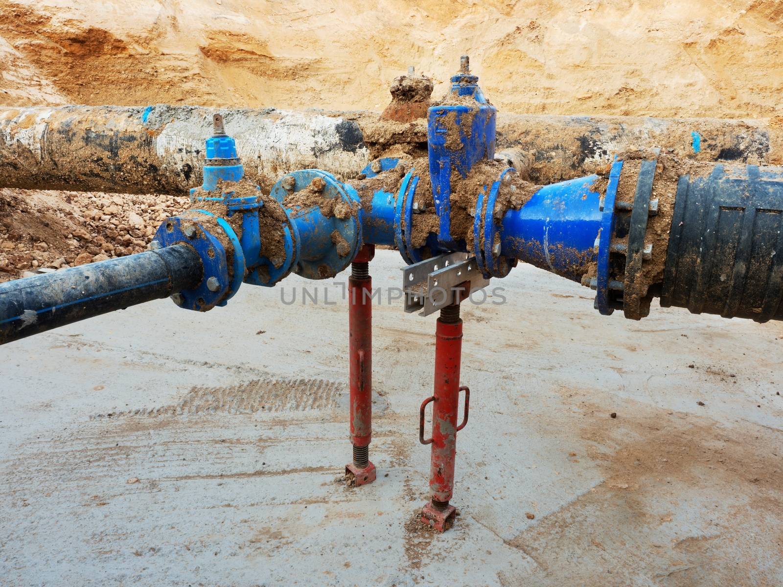 Old big drink water pipes joined with new blue gate valves and reduction joint members. Finished repaired piping waiting for covering by clay. Extreme kind of corrosion, metal corroded texture.