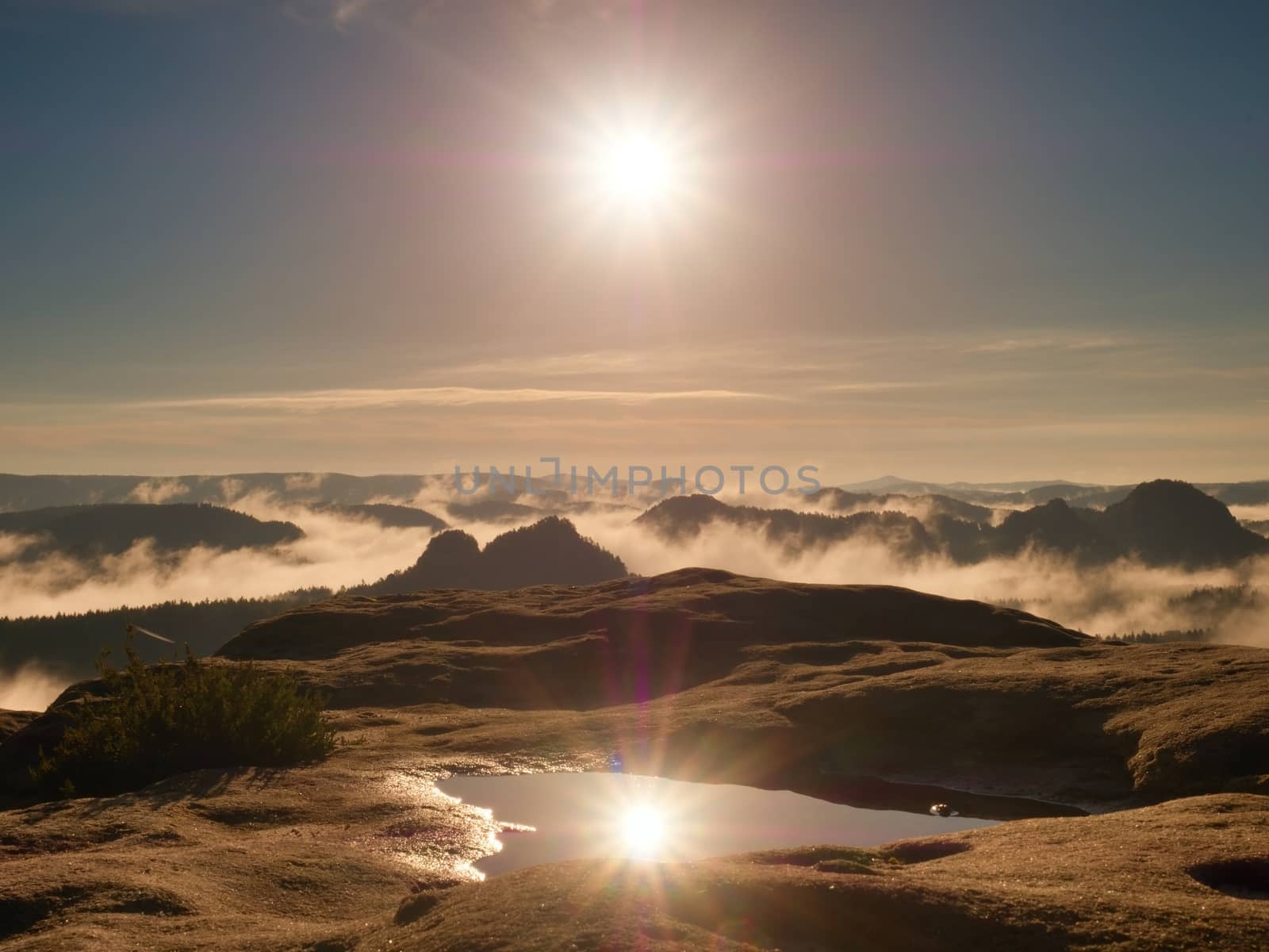 Water pool on cracked mountain summit.  Fairy daybreak in beautiful hills. Peaks of hills are in  yellow and orange fog stripped sun rays.