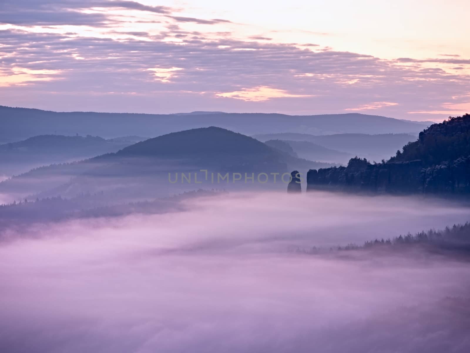 Pink daybreak in hilly landscape. Autumn misty morning in a beautiful rocky  hills. Peaks of hills are sticking out from fog. Miracle of nature