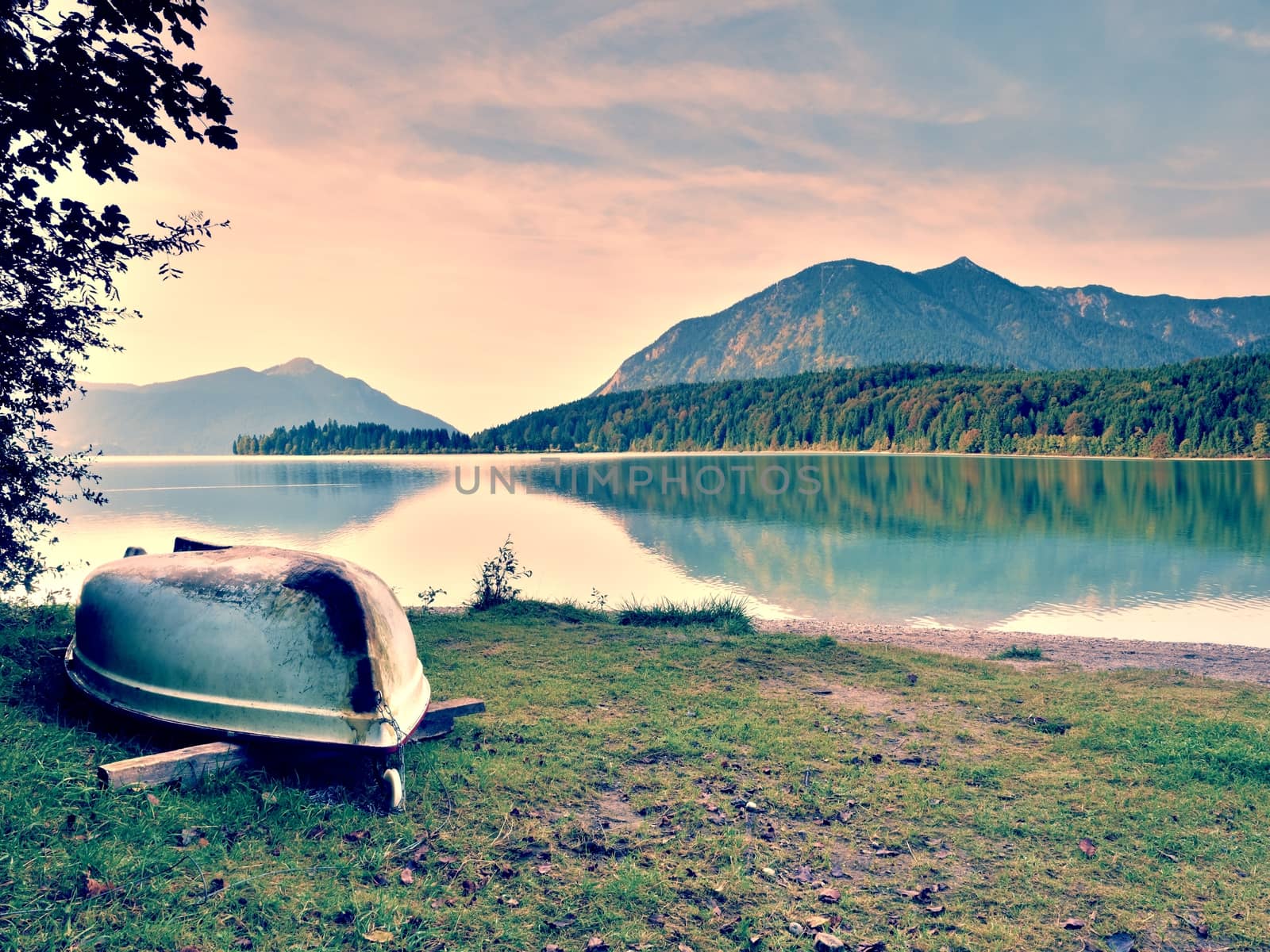 Upside down  fishing paddle boat on bank of Alps lake. Morning autumnal lake. Dramatic and picturesque scene. Mountains in water mirror.