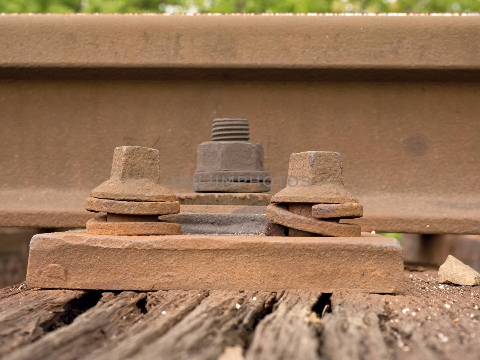 Detail of rusty screws and nut on old railroad track. Rotten wooden tie with rusty nuts and bolts. Damaged wooden railway sleeper. No train passed this railroad for a long time.