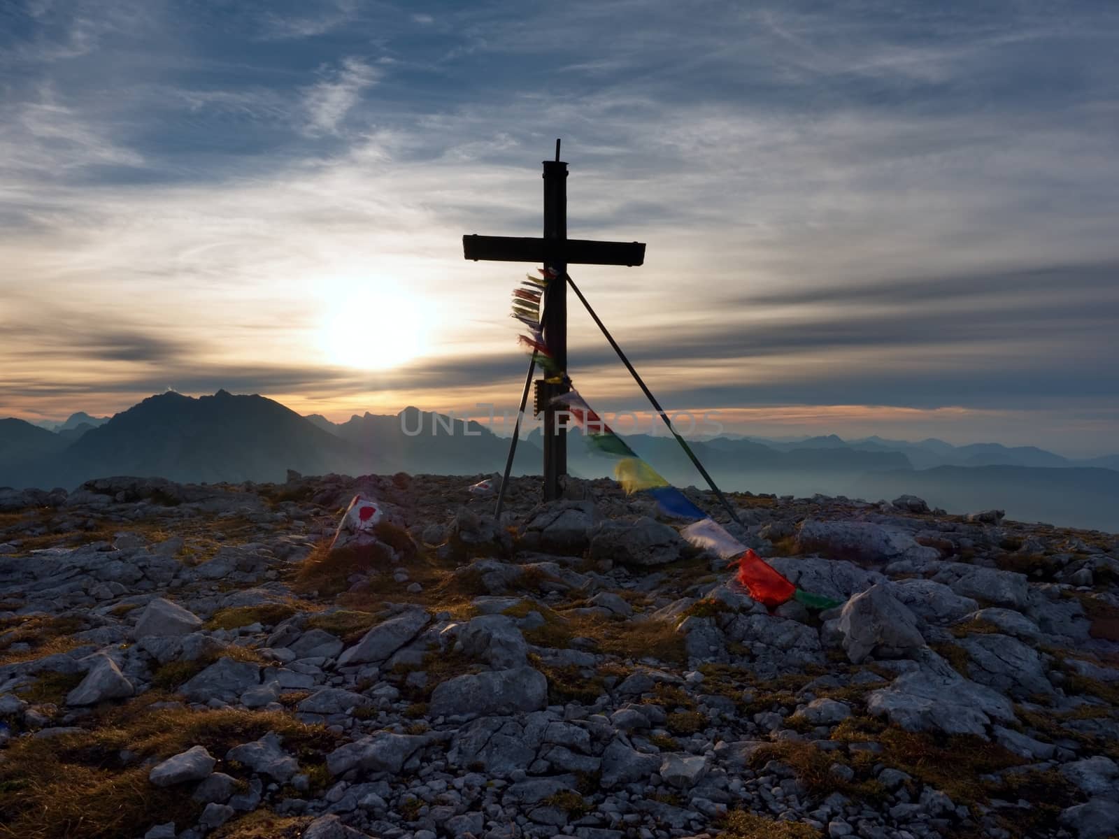 Big wooden cross at mountain peak in wind with Buddhist praying flags.  Cross on top of a mountains peak as typical in the Alps. Monument to the dead climbers