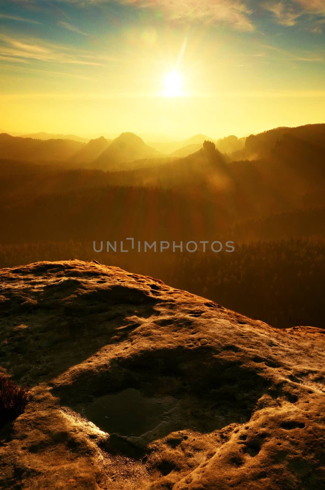 Sunrise in a beautiful mountain of Czech-Saxony Switzerland. Sandstone peaks increased from foggy background, the fog is orange due to sun rays. 