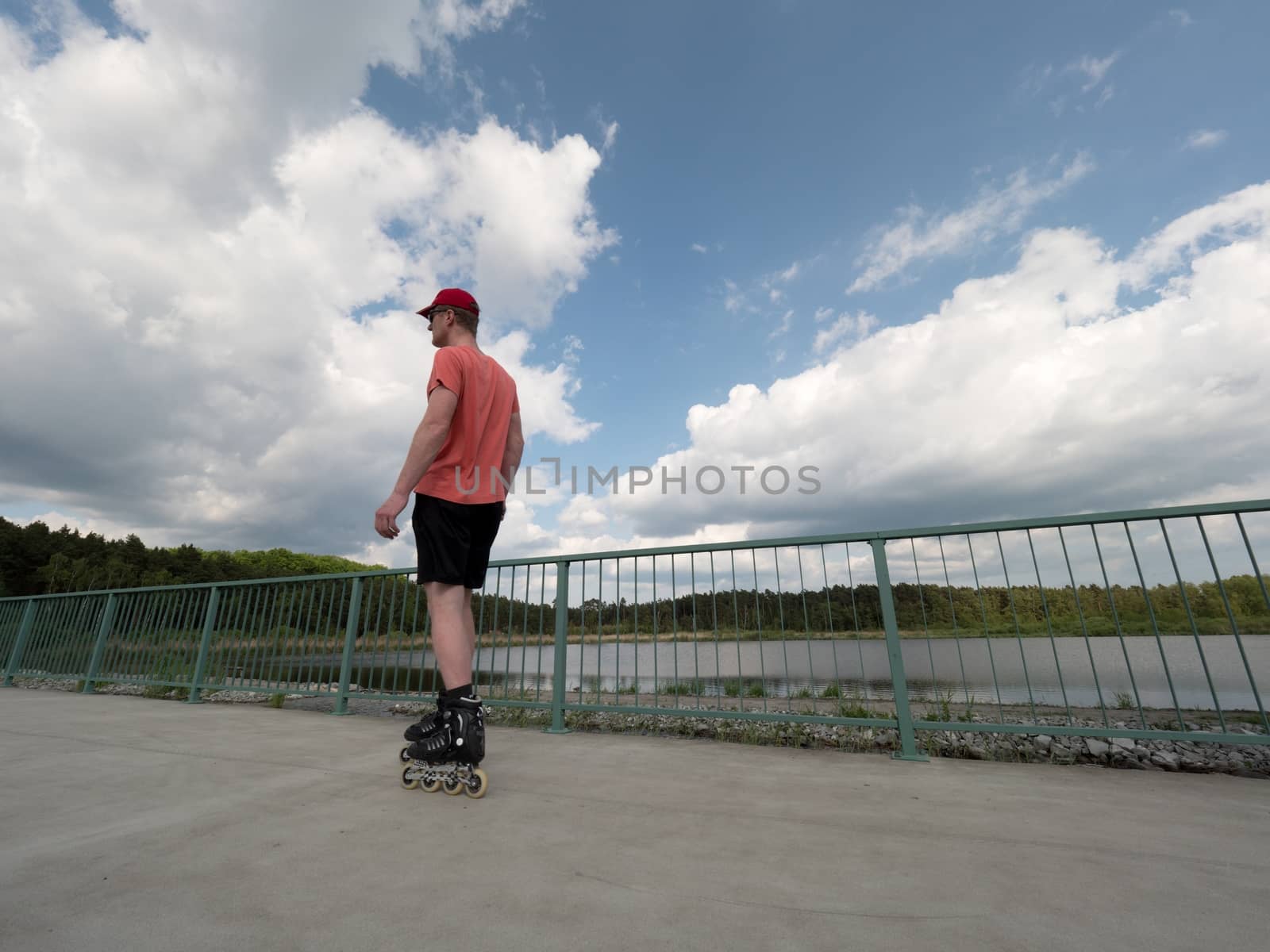 Roller skater in action. Man ride in inline skates ride along promenade handrail, blue sky in background. Low angle view