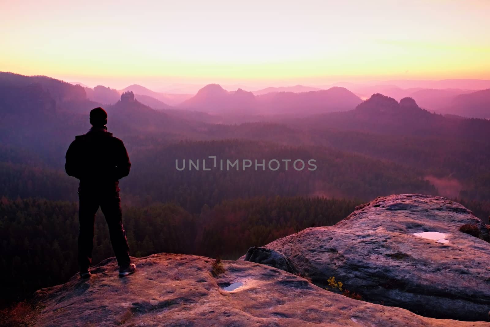 Tall man in black on cliff and watch to mountain sunrise.Silhouette in selfconfident pose.  Dark silhouette of rocks.