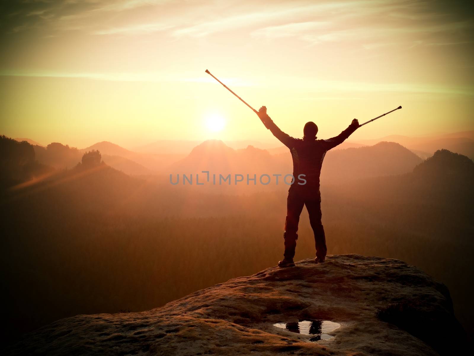 Happy man with broken leg and medicine crutch.  Hiker with leg in immobilizer achieve peak of mountain. Daybreak misty valley bellow silhouette. 