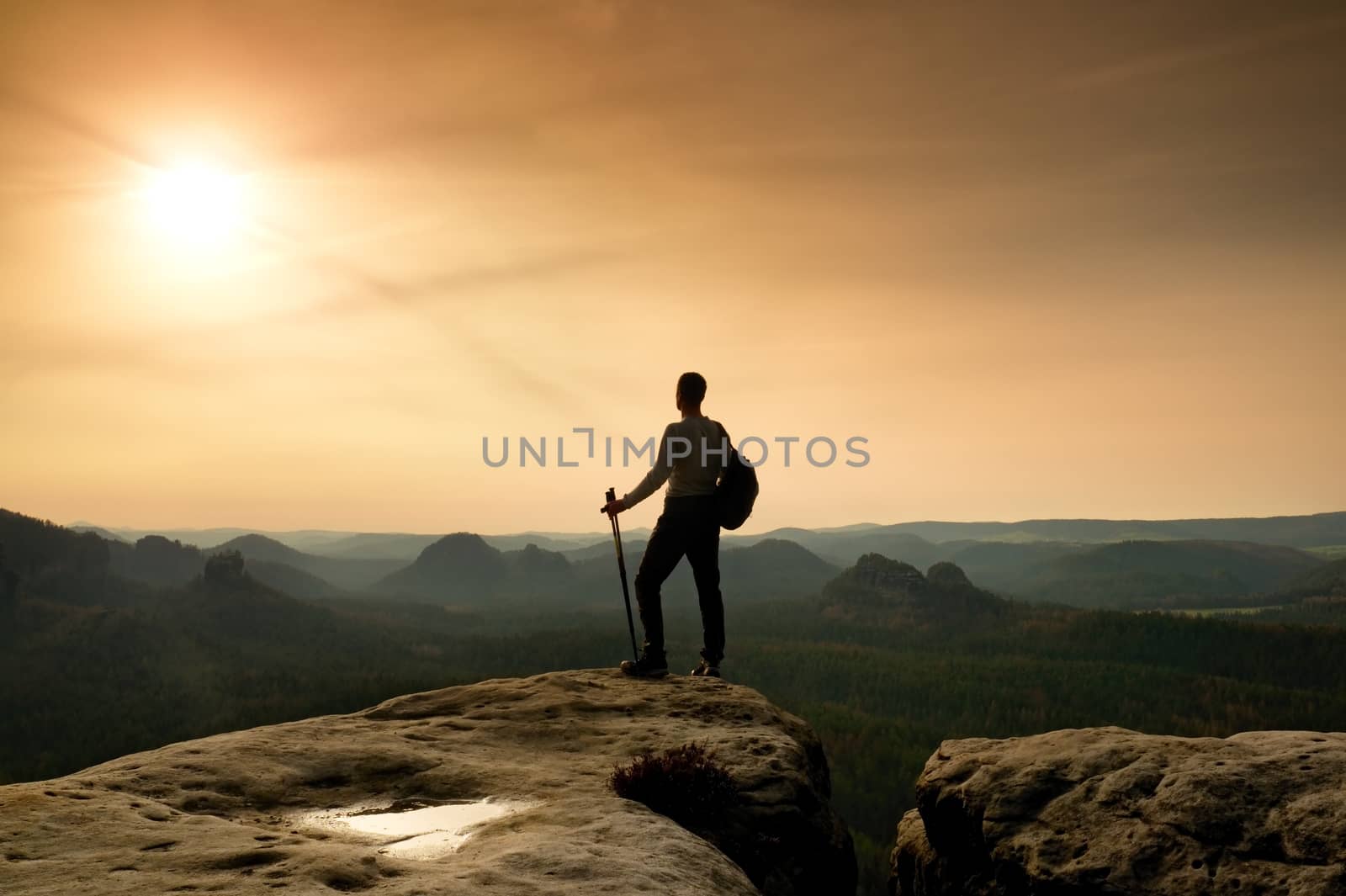 Silhouette of tourist. . Hiker with sporty backpack on rocky view point enjoying view into misty valley. Sunny spring daybreak in rocky mountains