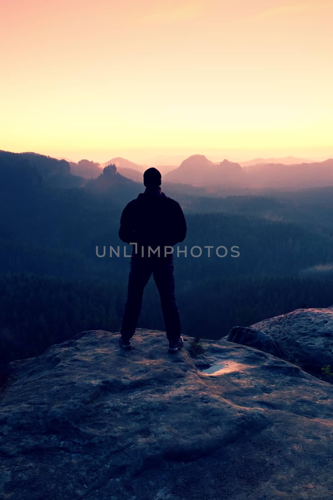 Tall man in black on cliff and watch to mountain sunrise.Silhouette in selfconfident pose.  Dark silhouette of rocks.