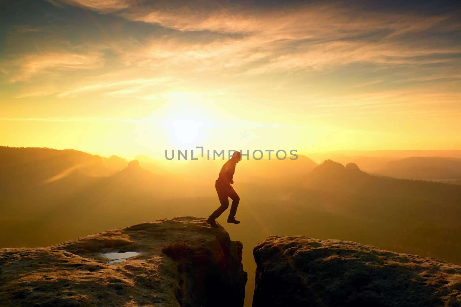 Young crazy man jump on mountain peak. Silhouette of jumping man and beautiful sunset sky. Vintage effect, lens defect.