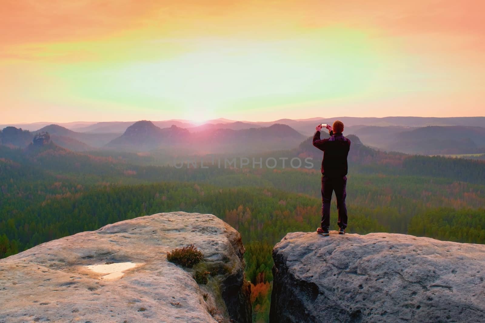 Man photography with phoneof  dreamy hilly landscape, spring orange pink misty sunrise in a beautiful valley of rocky mountains.