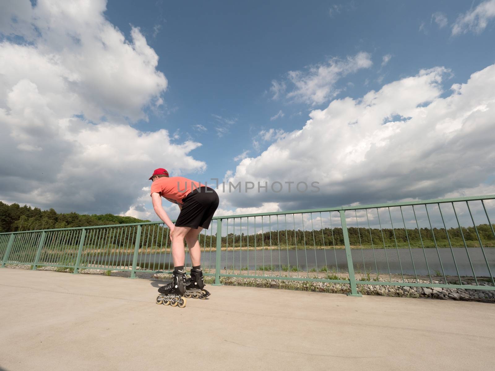 Middle age man in red t-shirt  with inline skates ride in summer park, popular outdoor skating.  by rdonar2