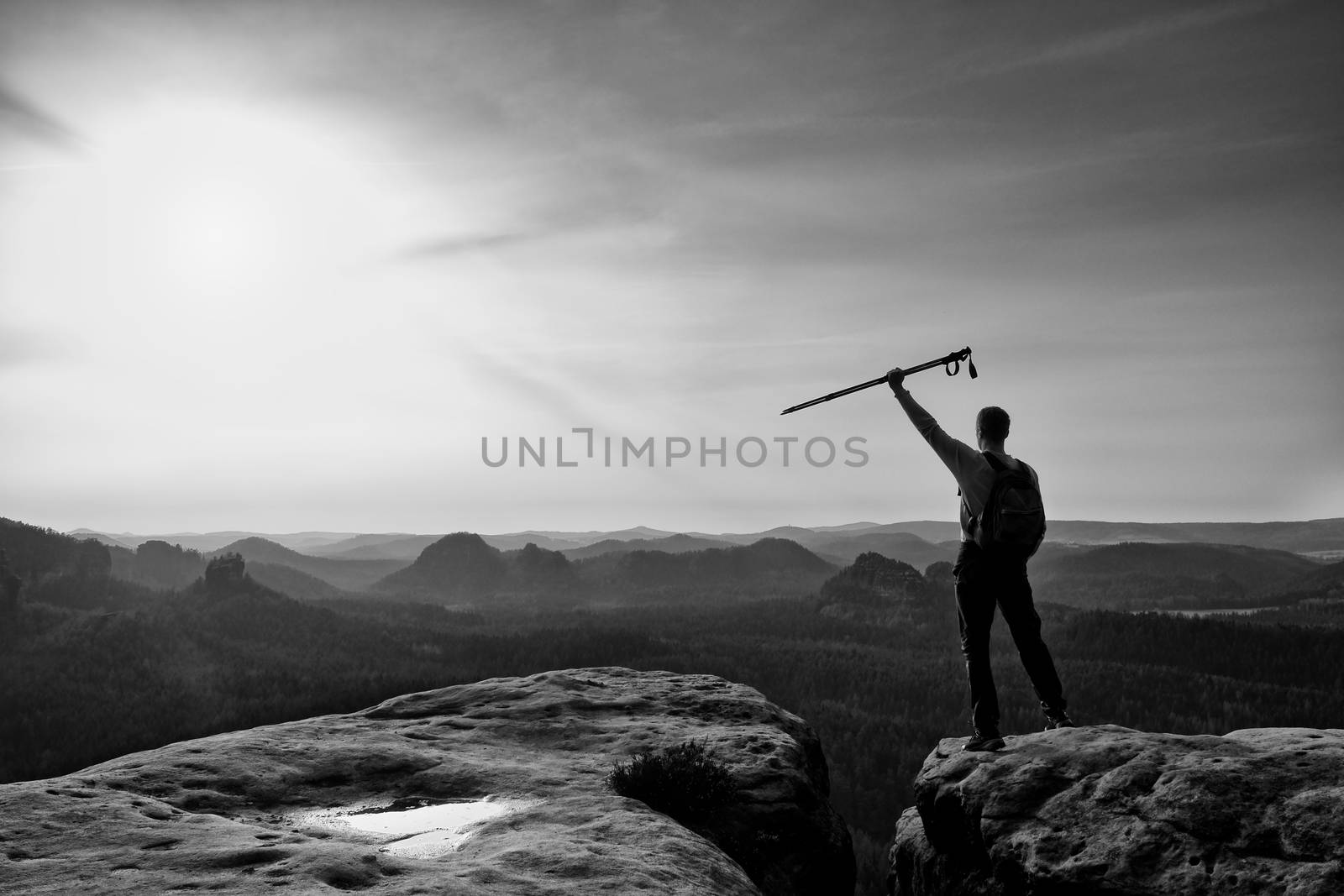 Tourist with poles in hands stand on rock watching  for next step. Sunny spring daybreak in mountains.Vignetting effect.. 