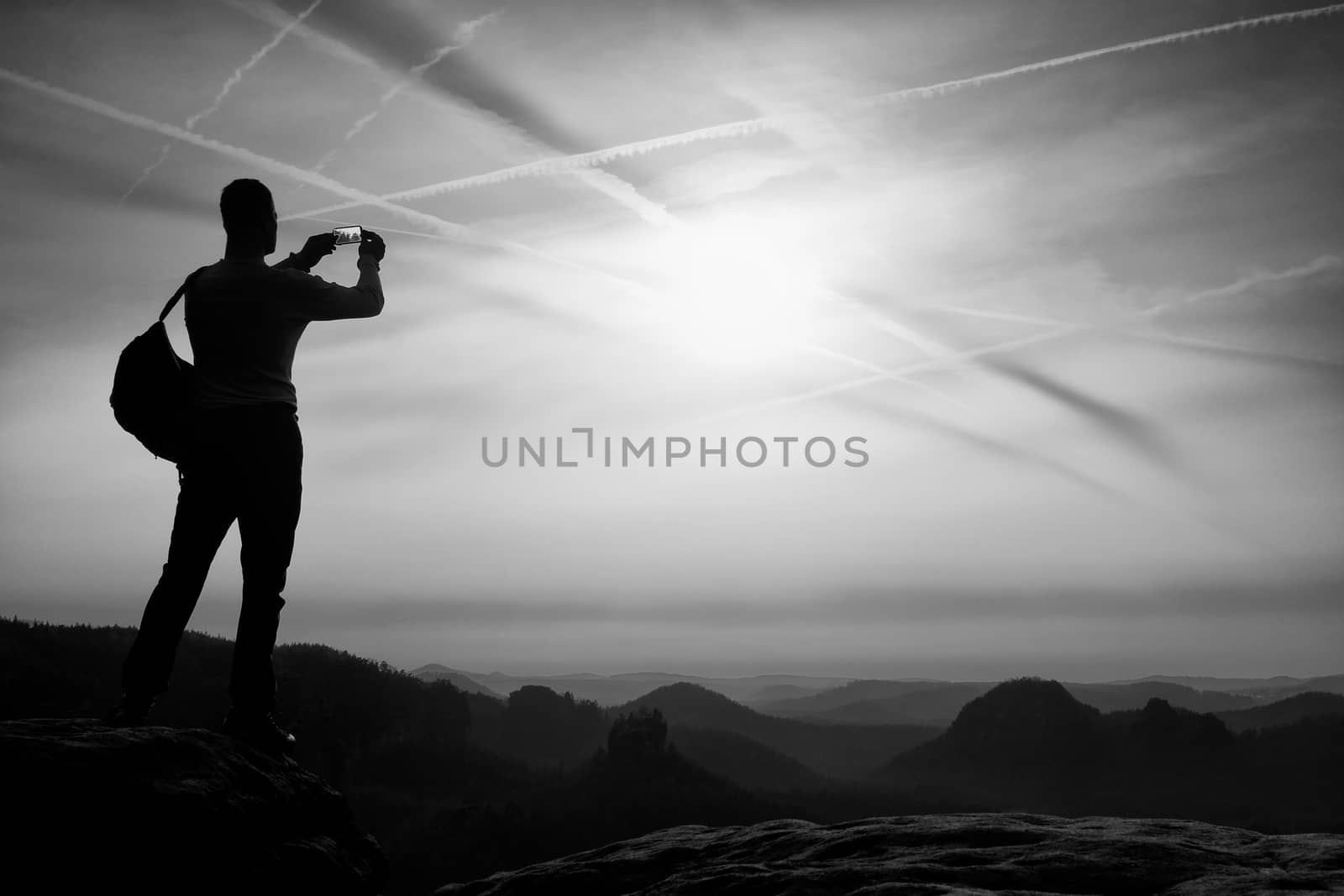 Hiker with backpack on sharp sandstone rock in rock empires park and watching over the misty and foggy spring valley to Horizon.