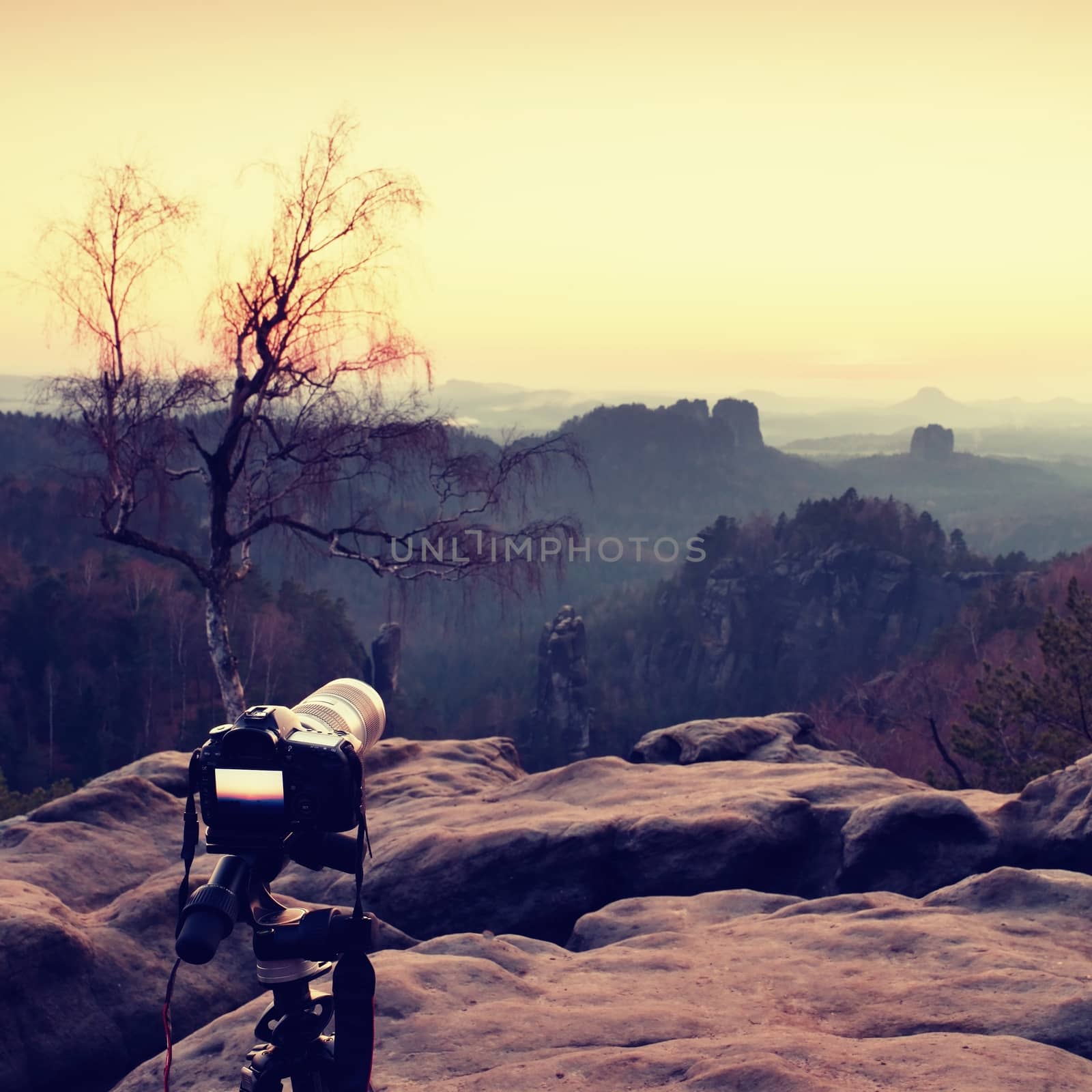 Tripod with big camera stand on mountain peak after sunset. Sharp sandstone cliffs at horizon