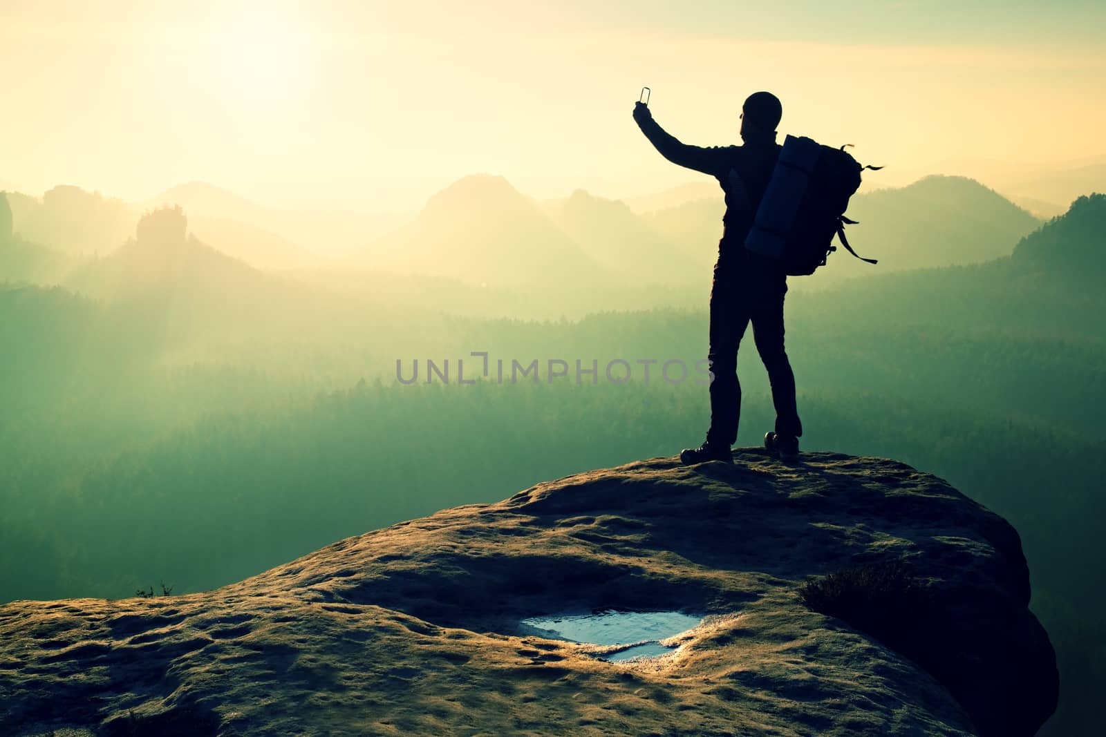 Strong man hiker taking photo with smart phone at mountain peak. Marvelous daybreak.