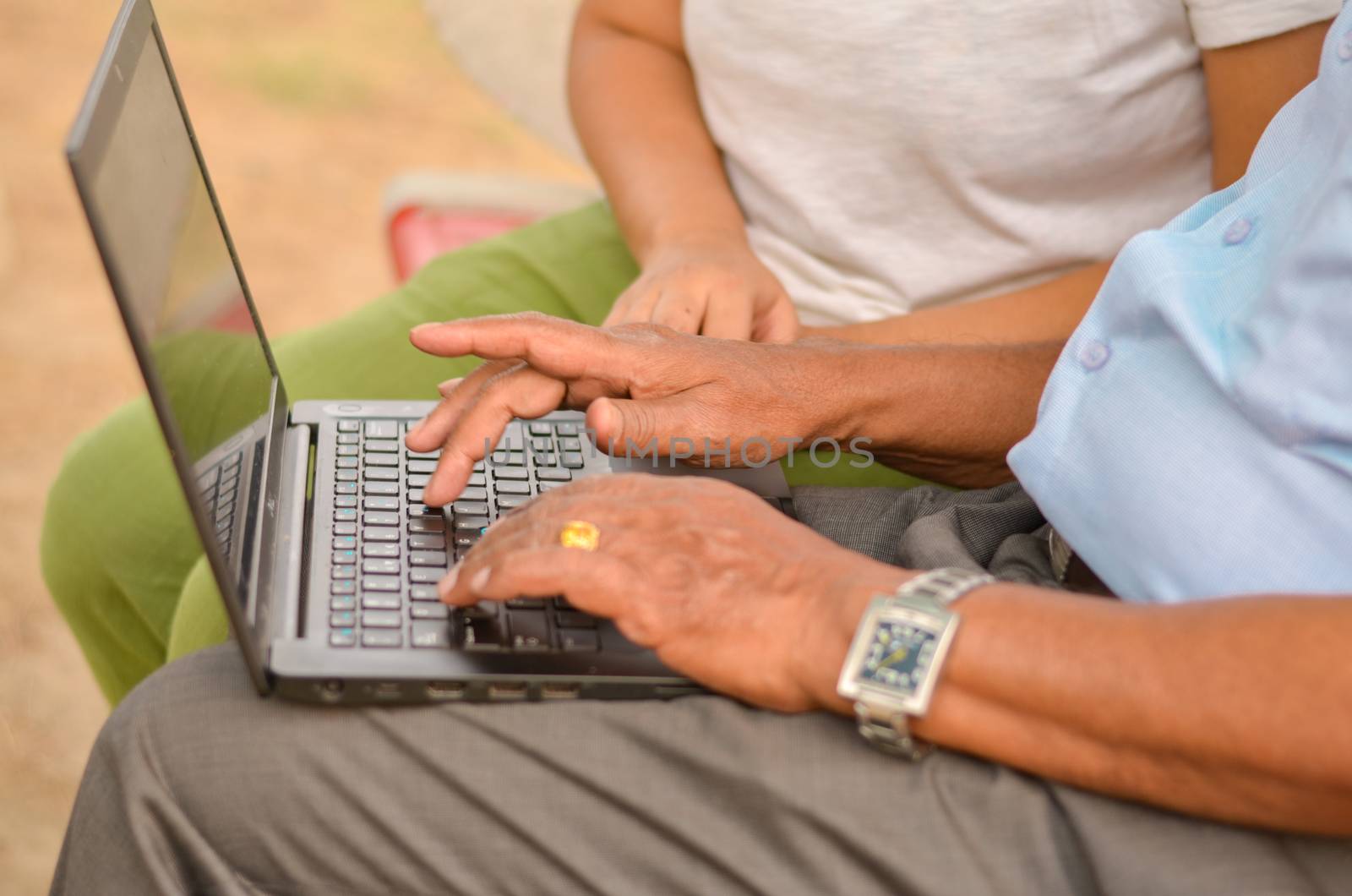 Side view close up of hands of an young Indian girl helping / teaching an old Indian woman on a laptop sitting on a red bench in a park in New Delhi, India