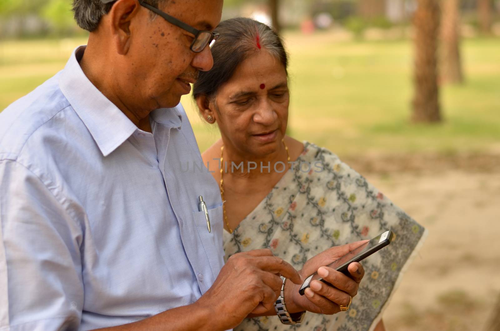 Senior Indian Bengali couple in park looking at their smart phone and smiling in a park in New Delhi, India. Concept love