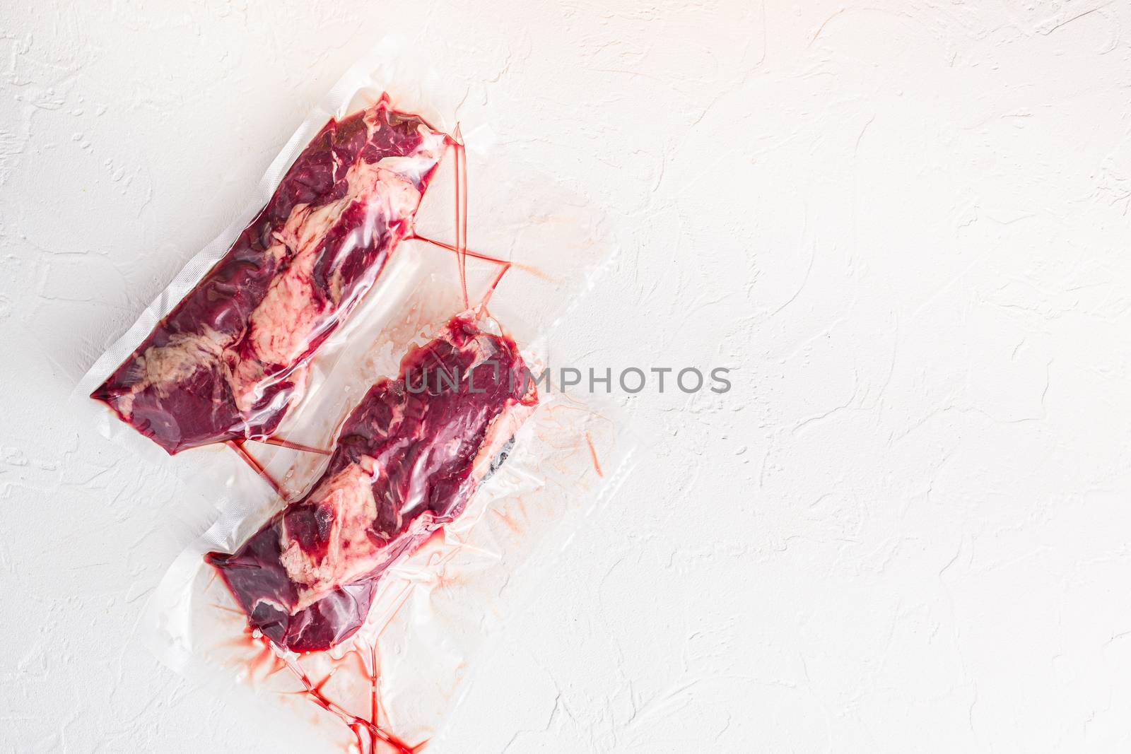 Pair of chuck roll beef steak, vacuum packed organic meat for sous vide cooking on white concrete textured background, top view space for text