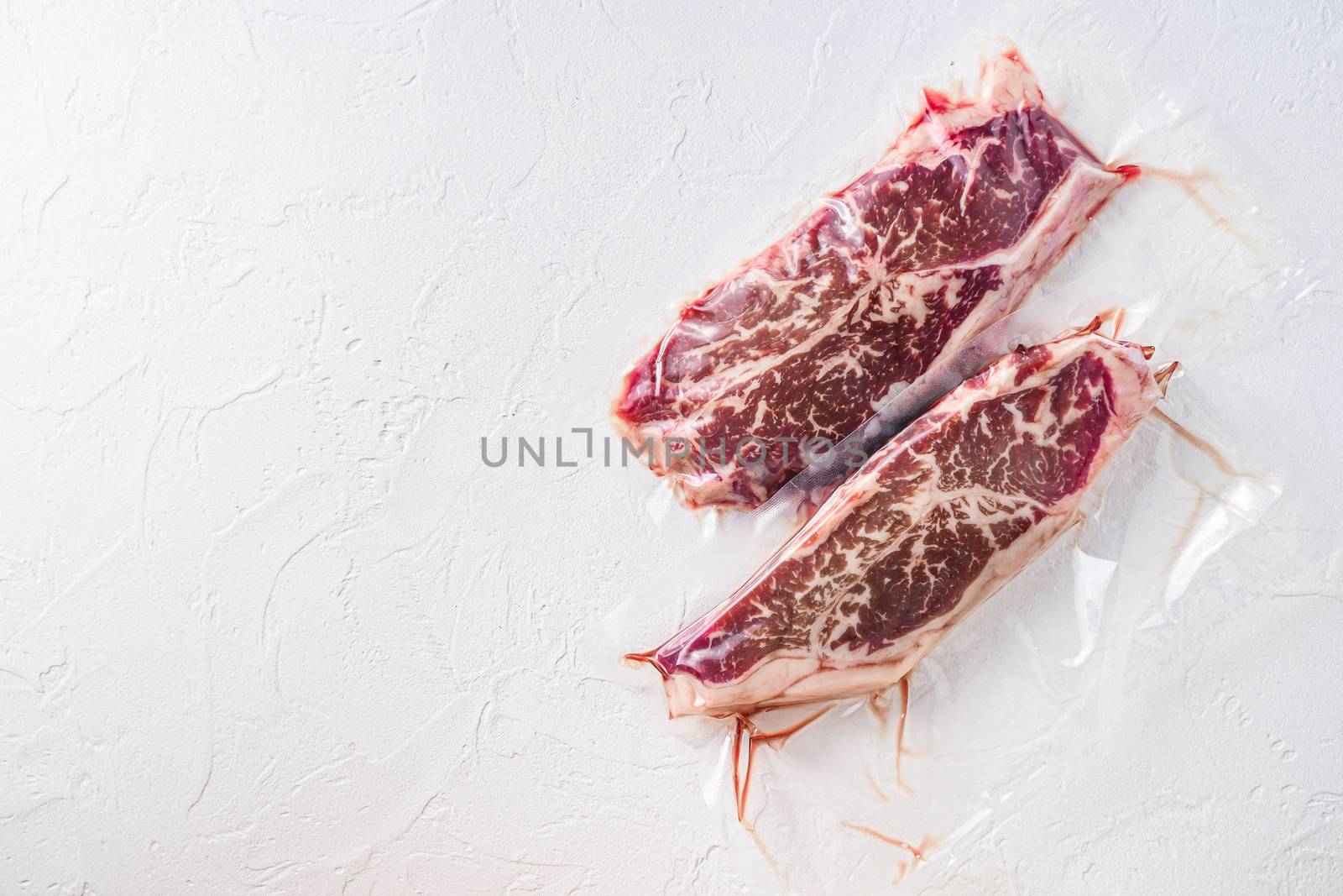 Top blade steak, vacuum packed organic beef meat on white concrete textured background, top view with space for text