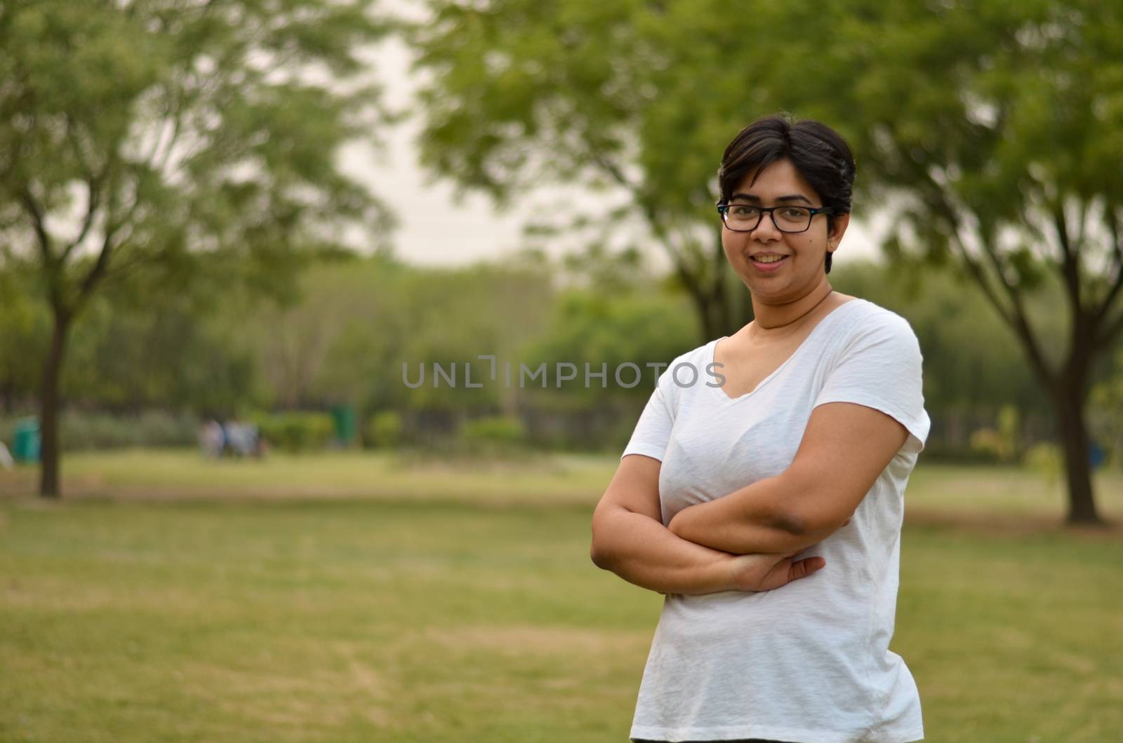 Smart Indian woman standing, posing for the camera with hands crossed / folded in a park wearing white in summers in New Delhi, India