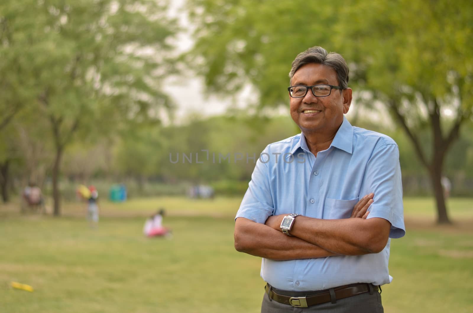 Portrait of a happy senior Indian man wearing a shirt and hands crossed in the outside setting standing and thinking in a park in New Delhi, India