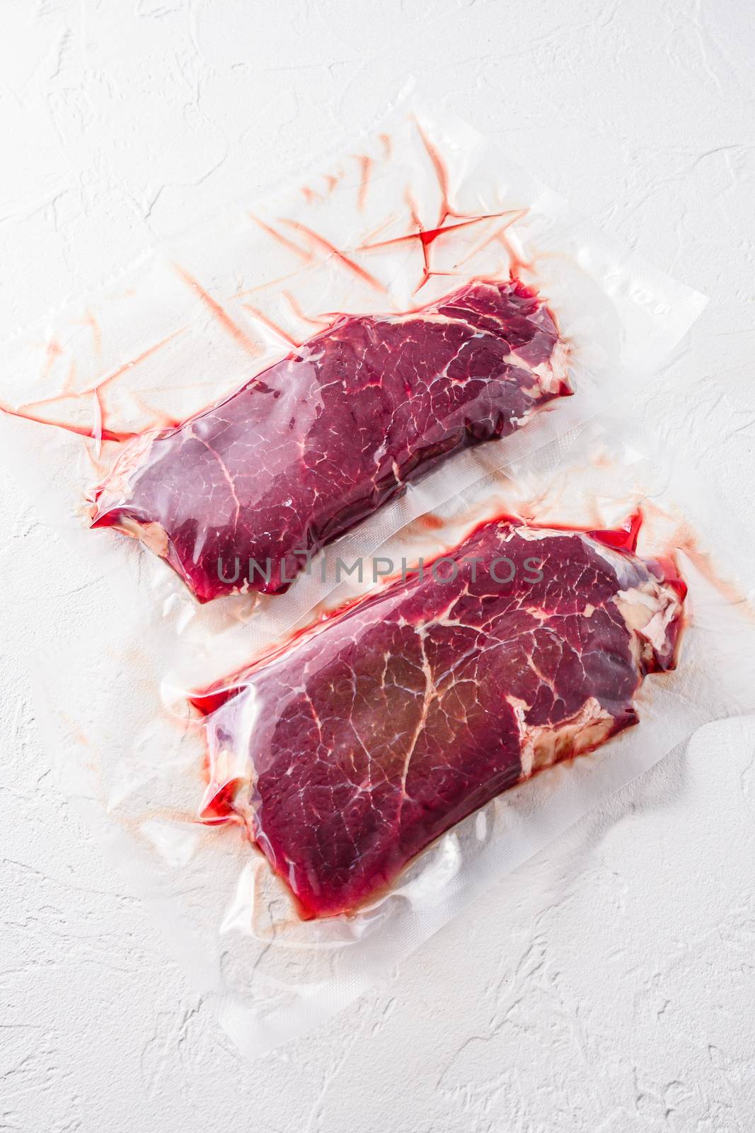 Set of vacuum packed organic beef meat rump steak on white concrete textured background, side view. by Ilianesolenyi