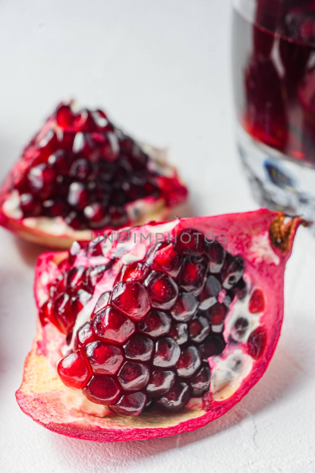 Pomegranate cut with seeds close up in front of garnet cut and juice in glass side view, selective focus by Ilianesolenyi