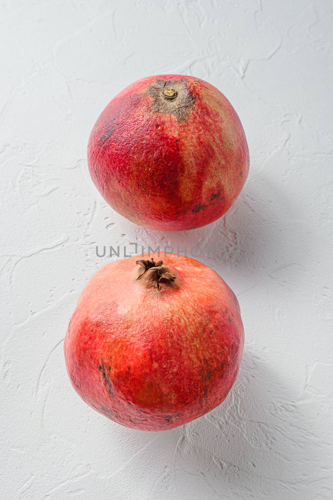 Fresh pair of pomegranate over white concrete background, side view. by Ilianesolenyi