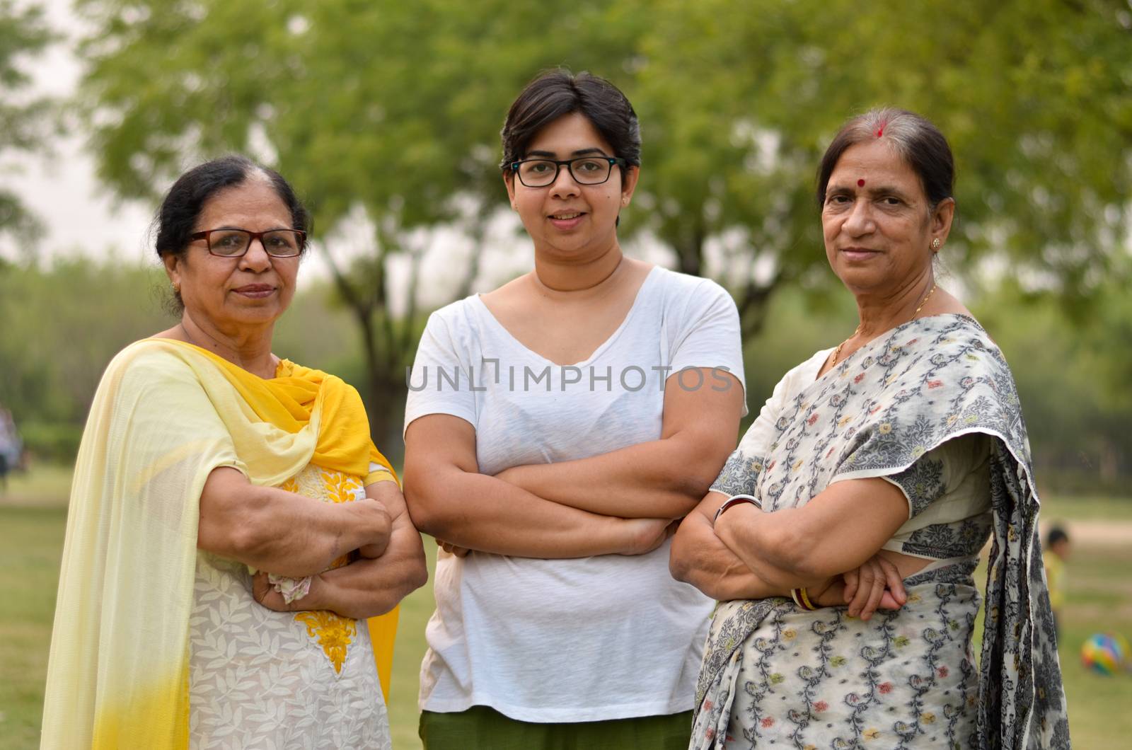 Portrait of two senior Indian women women standing with their daughter / daughter-in-law in a park wearing saree and salwar kamiz with crossed / folded hands during winters in New Delhi, India by jayantbahel