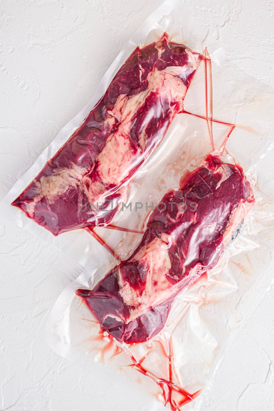 Pair of chuck roll beef steak, vacuum packed organic meat for sous vide cooking on white concrete textured background, top view