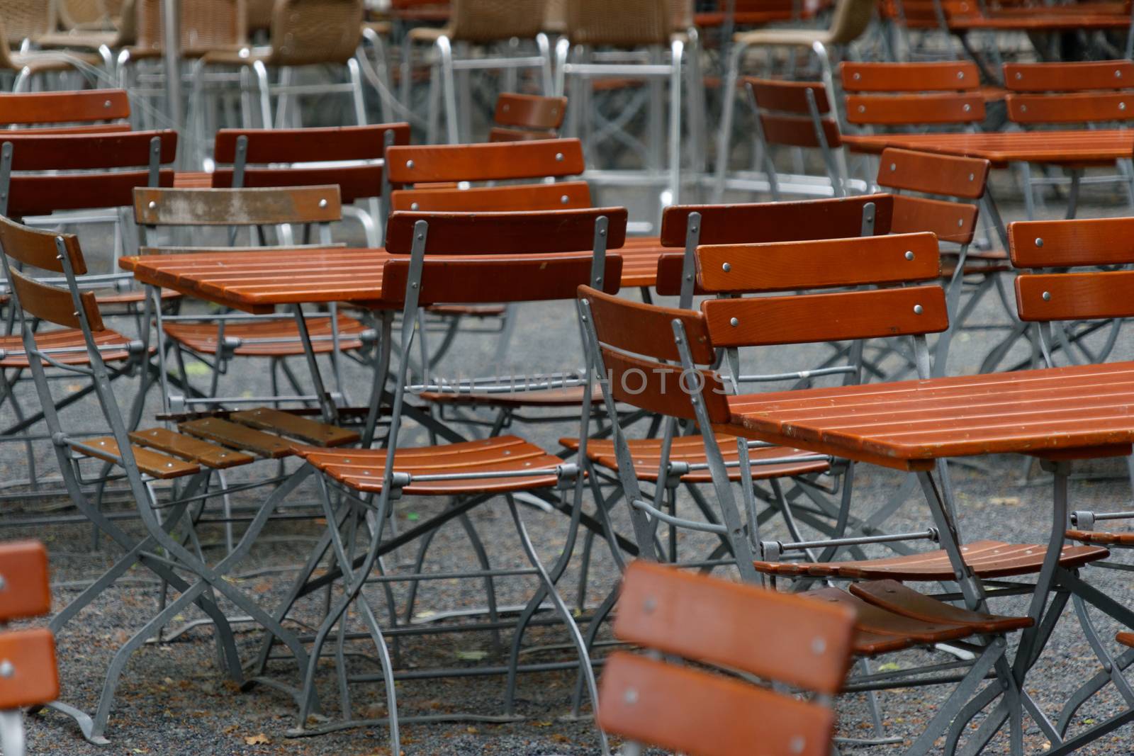 Unoccupied chairs and tables in a garden restaurant with table legs and chair legs made of iron and wooden tops by geogif