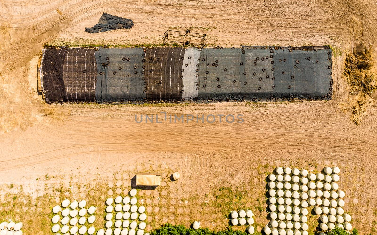 Aerial view of a farm warehouse, vertical photographed round silage bales wrapped in foils, made with drone