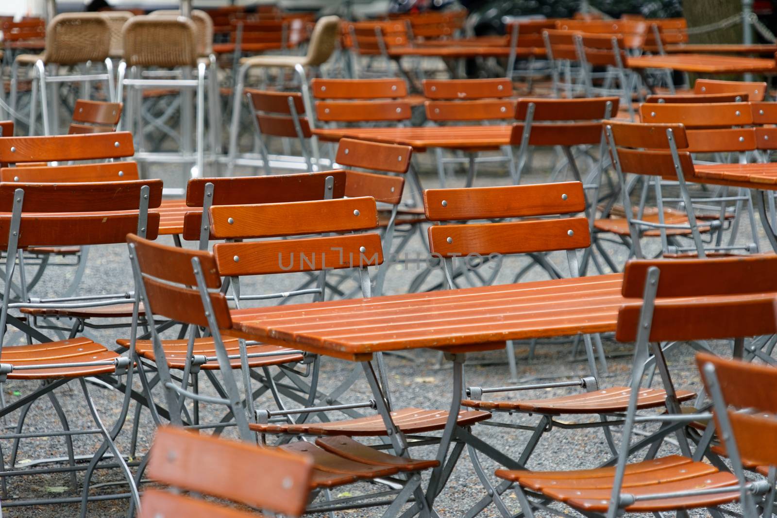 Unoccupied chairs and tables in a garden restaurant with table legs and chair legs made of iron and wooden tops, Germany